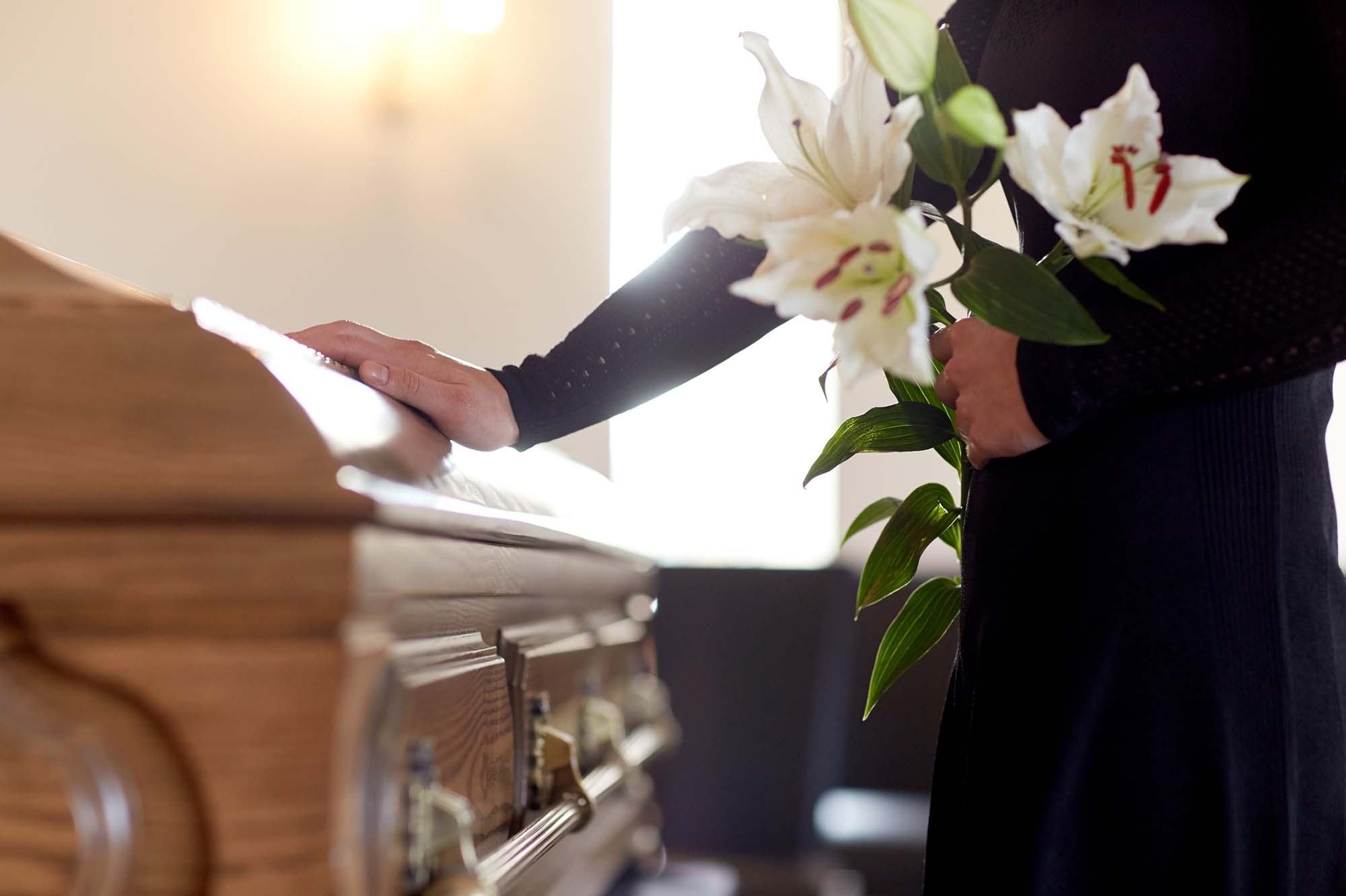 Woman holding a bunch of Lilies at a coffin
